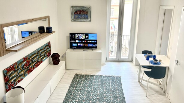 Un salon moderne doté d’un téléviseur à écran plat, d’un coin repas avec une table et des chaises, d’un tapis à motifs et d’un balcon offrant une vue agréable.