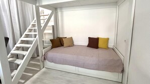 Une chambre à coucher de taille réduite, dotée d’un lit intégré, d’un escalier blanc et d’un mur blanc uni.