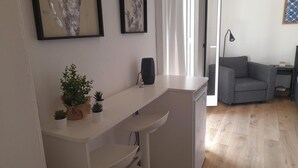 A modern living room with a white sofa, a grey armchair, and a small table with plants. There are framed pictures on the wall and a lamp on a side table. - Circe Studio Sea View (Syracuse)