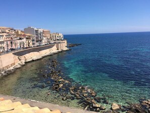 A coastal town with buildings along the sea, clear water, and rocky shoreline. - Circe Studio Sea View (Syracuse)