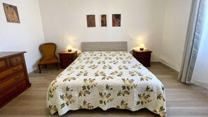 A bedroom with a bed, two nightstands, a chair, a dresser, and three framed pictures on the wall. - Casa La Palma in San Giuliano Terme (Vecchiano)