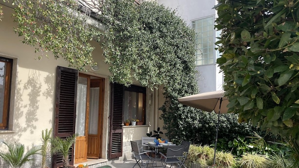 A patio with a table and chairs, surrounded by potted plants and a large tree. - Casa La Palma in San Giuliano Terme (Vecchiano)