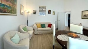 A living room with a sofa set, a dining table with a doily, and a floor lamp. - Casa La Palma in San Giuliano Terme (Vecchiano)
