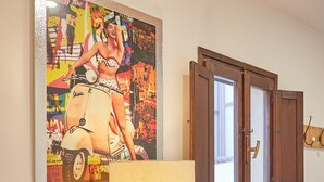 A room with a wooden cabinet, a lamp, a framed artwork, and a window with wooden shutters. - Cala Rossa in Siracusa (Syracuse)
