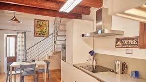A modern kitchen with a stainless steel kettle, a coffee sign, and a staircase leading to another room. - Cala Rossa in Siracusa (Syracuse)