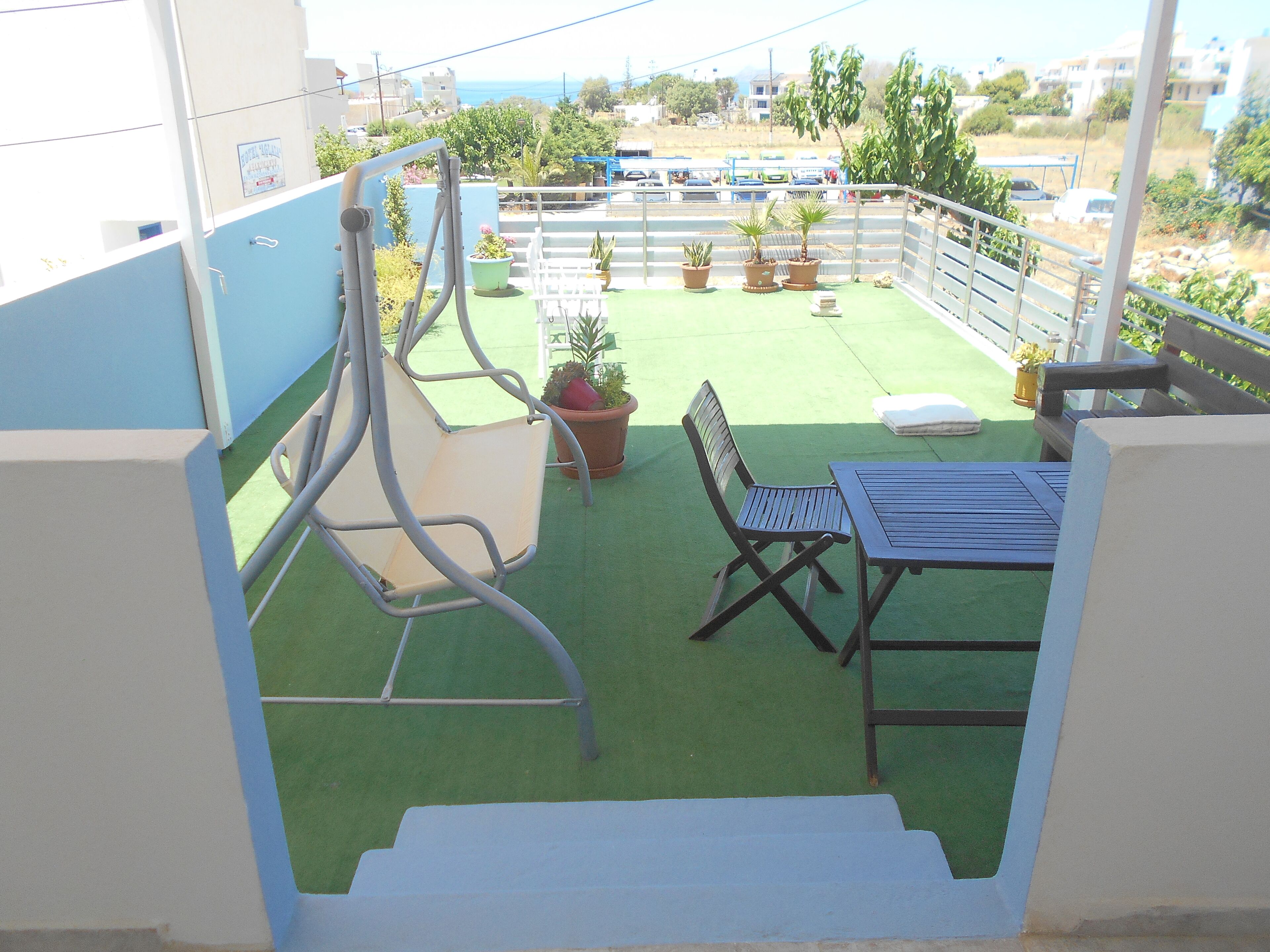 A balcony with a green artificial turf, a metal chair, a table, and several potted plants.
