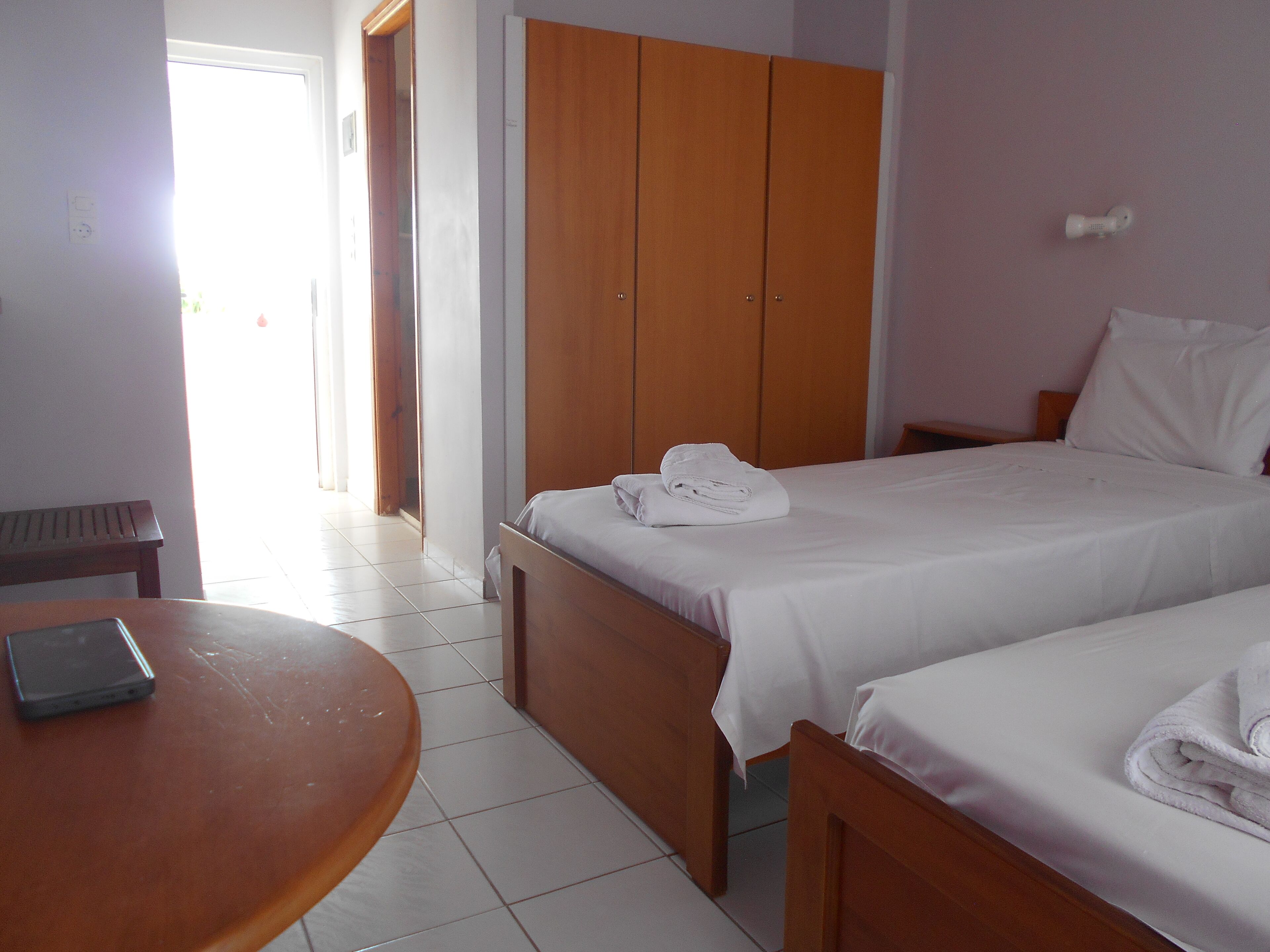 Habitació d'hotel amb dos llits, un armari de fusta, una taula petita amb un ordinador portàtil i una banca.