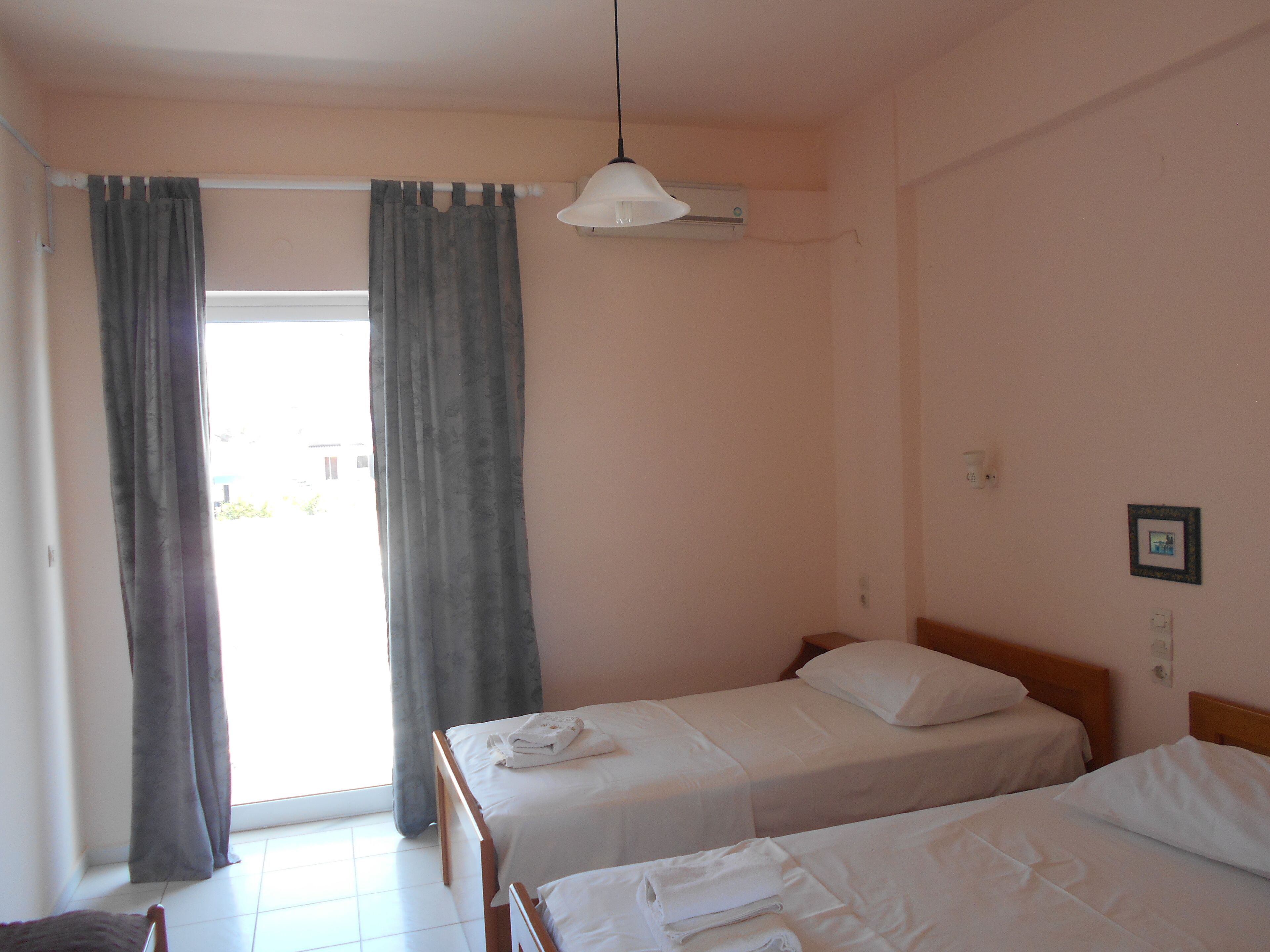 Habitación de hotel con dos camas individuales, ventilador de techo y ventana con cortinas.