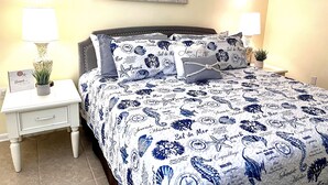 A bedroom with a bed covered in a blue and white nautical-themed bedspread, two bedside lamps, a small potted plant, and a framed picture on the wall. - Ocean Village Club-Sleeps 4 with First  Floor Access and Screen Porch (St. Augustine)