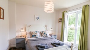 Et pænt arrangeret soveværelse med en seng, to sengeborde, en hængende lampe, et vindue med gardiner og et billede på væggen.