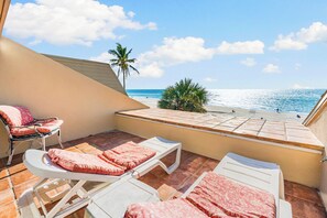 A balcony with two white lounge chairs, one with a pink cushion and another with a red patterned cushion.