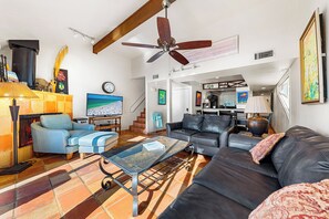 A spacious living room with a fireplace, a ceiling fan, and a large window.