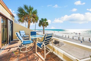 A balcony with a view of the beach, featuring lounge chairs and a table.