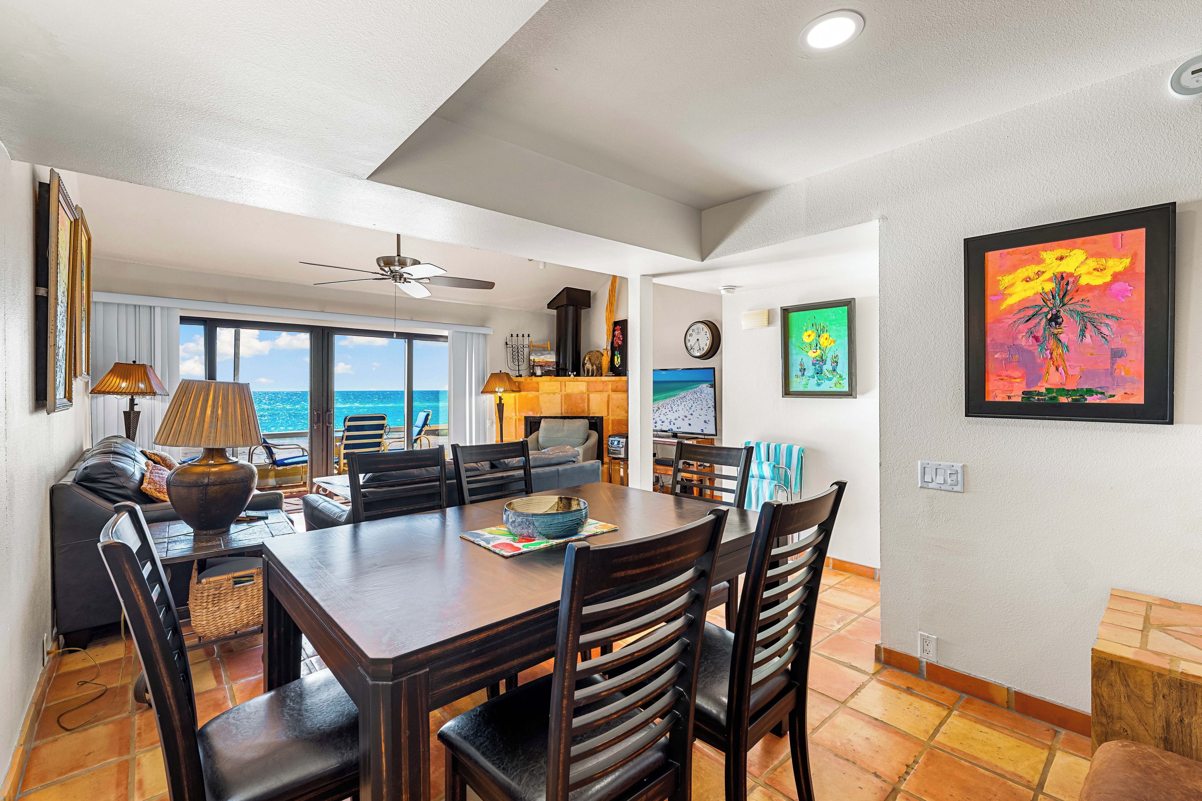A dining area with a large table, chairs, and a view of the ocean through large windows.