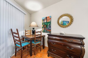 A dining area with a wooden table, chairs, a lamp, a dresser, and a painting on the wall.
