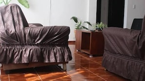 A living room with a brown leather sofa, a television on the wall, and a 'HOME' mat on the floor.