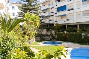 A residential building with multiple balconies, a swimming pool, and lush greenery.
