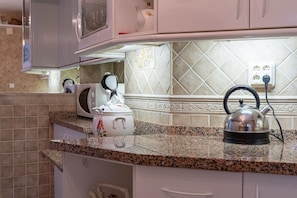 A kitchen with granite countertops, a kettle, a microwave, and a cabinet with a decorative item.
