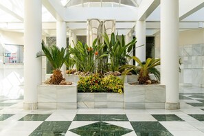 A lobby with marble flooring, white columns, and tropical plants.
