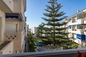 A residential building with balconies, a swimming pool, and a large pine tree.