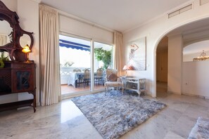 A spacious room with a large sliding glass door leading to an outdoor area, a classic wooden sideboard, a fluffy rug, and a chandelier.
