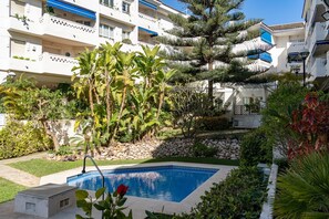 A residential building with a swimming pool surrounded by tropical plants and a stone wall.