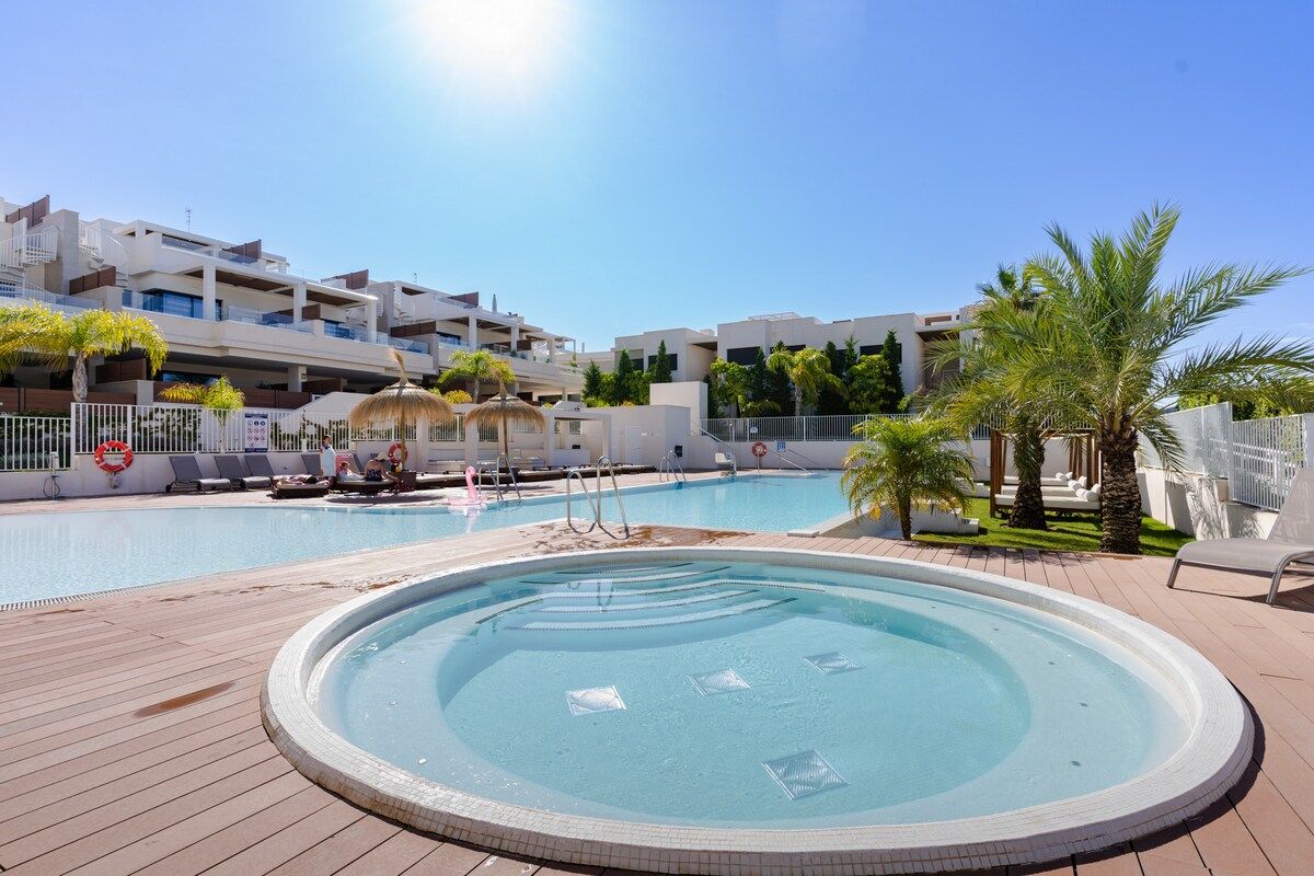 A swimming pool area with a hot tub, lounge chairs, and a palm tree.