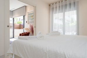 A hotel room with a large bed, a view through a glass door, and a window with sheer curtains.