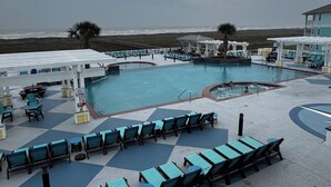 Zona de piscina con sillas de descanso y un jacuzzi, rodeada por una pérgola blanca y una palmera.