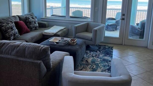 Salón con vista al océano, que incluye un sofá, sillones, una mesa de centro y un ventanal grande.