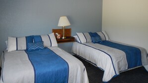 A hotel room with two single beds, a nightstand with a lamp, and a small table with a tissue box.