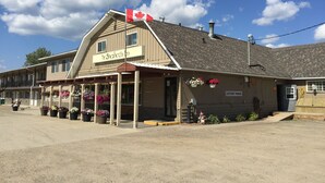 A two-story building with a sign reading "The Shepherd's Inn." There are flower baskets hanging outside and a Canadian flag on top. - The Shepherd's Inn (Charlie Lake)