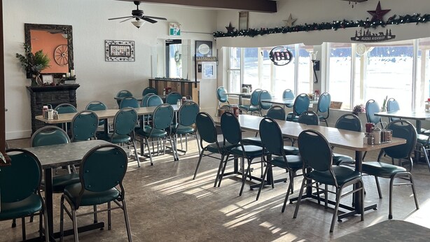 A spacious dining area with multiple tables and chairs, ceiling fans, and a view of the outside. - The Shepherd's Inn (Charlie Lake)