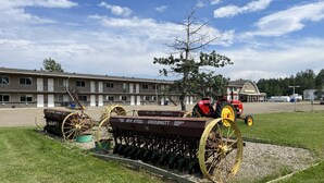 A motel with a large parking lot, a red tractor, and agricultural equipment. - The Shepherd's Inn (Charlie Lake)