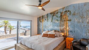 A bedroom with a large bed, a ceiling fan, and a view of the sea through a sliding glass door. - Jet Boat Billy's Speed Shop Havasu (needles)