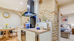 Una cucina moderna con parete a tema in pietra, una zona pranzo con tavolo rotondo e una camera da letto con letto e quadro.