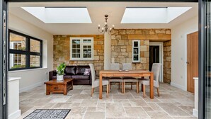 Un espace patio accueillant agrémenté d’un mur en pierre, d’un canapé en cuir, d’une table en bois avec des chaises et d’un lustre.
