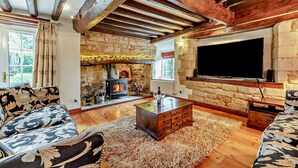 Un salon chaleureux avec une cheminée en pierre, des poutres en bois, un canapé et un téléviseur.