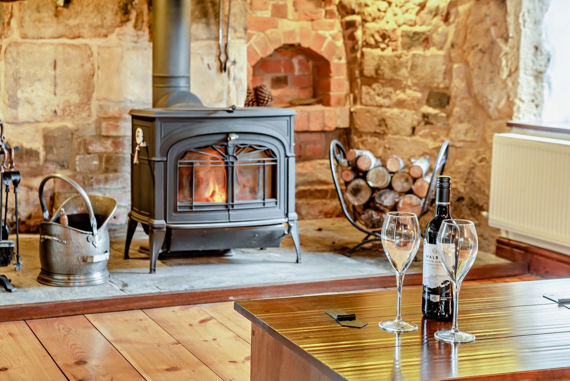 Une pièce chaleureuse avec un poêle à bois, une bouilloire en métal et une table avec des verres à vin.