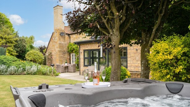 Un bain à remous rempli d’eau, une bouteille de vin et une table avec des chaises, le tout installé dans un coin du jardin.