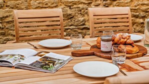 A wooden table with a stone wall background, featuring a croissant, a jar of jam, and a magazine.
