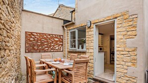 A cozy outdoor dining area with a stone wall, wooden chairs, and a table set for two.