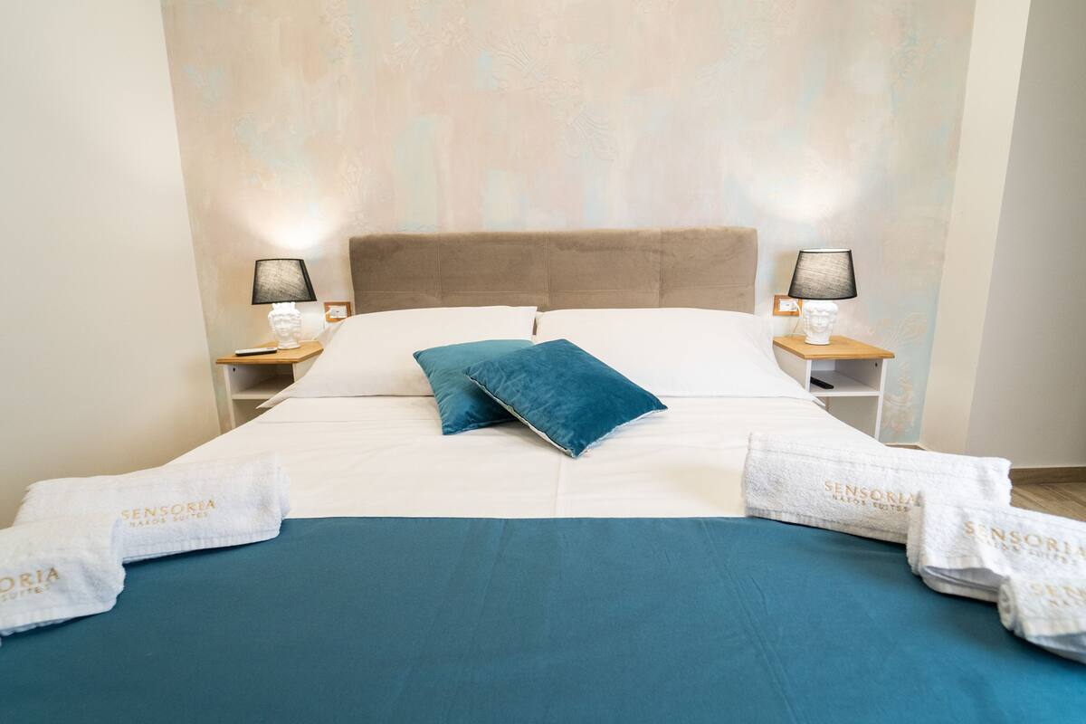 A neatly made bed with white and blue bedding, two bedside lamps, and a headboard.