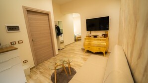Un salon moderne avec un canapé, une table basse en verre, une commode jaune et un téléviseur à écran plat fixé au mur.