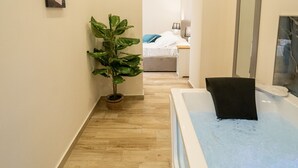 Un couloir avec un plancher en bois, une plante en pot, une baignoire et un lit à l’arrière-plan.