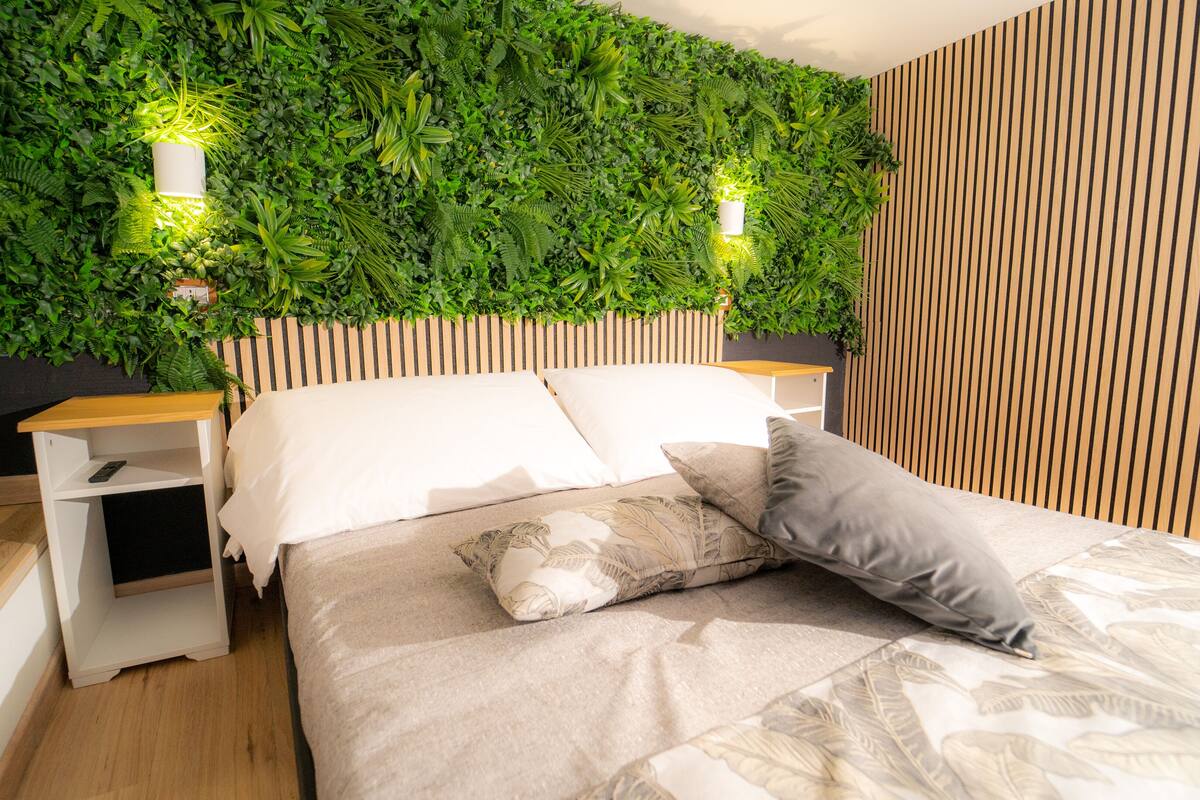 A modern bedroom with a green wall, wooden headboard, and a bed with white and grey bedding.