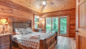 A wooden cabin bedroom with a bed, bedside tables, and a ceiling fan. - Magical Metamora Cottage w/ Fire Pit, Pond, Deck! (Metamora)
