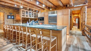 A wooden cabin interior with a kitchen featuring a central island with bar stools, built-in cabinets, and a stainless steel refrigerator. - Magical Metamora Cottage w/ Fire Pit, Pond, Deck! (Metamora)