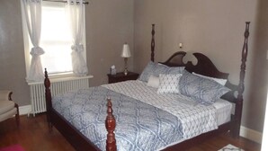 A bedroom with a four-poster bed, a bedside table with a lamp, a radiator, and a chair. - Windsor Lofts 2 (Roanoke)