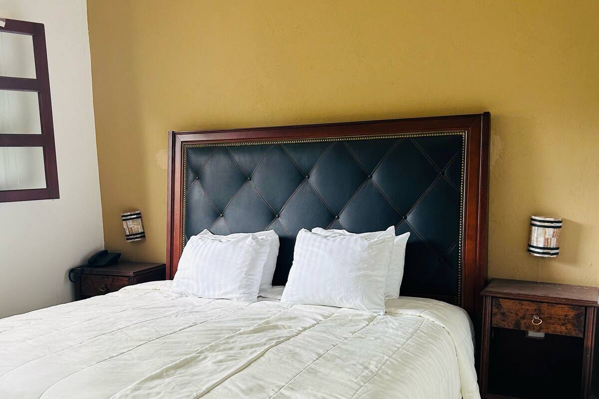 Una cama bien tendida con cabecera capitonada, ropa de cama blanca y dos mesitas de noche con lámparas.